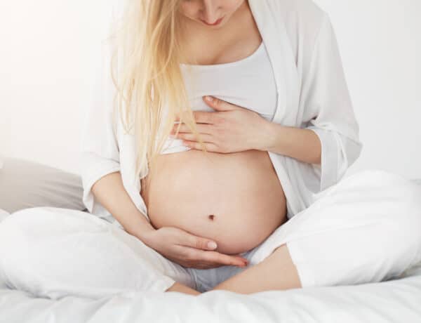 Femme enceinte assise sur un lit, les mains posées sur son ventre